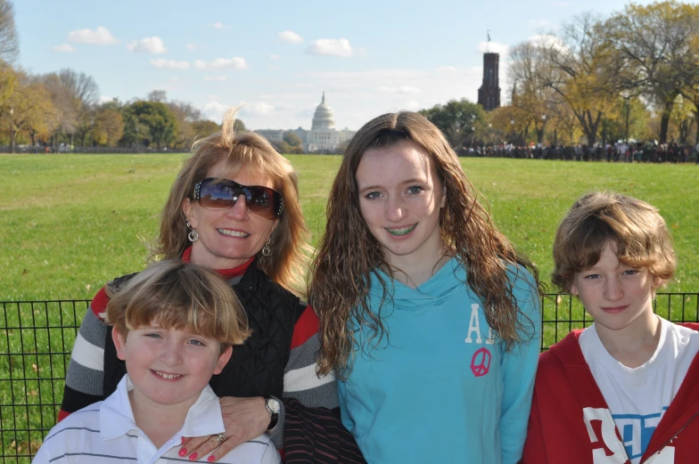 three children standing next to an adult in a grassy area