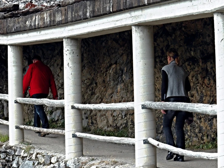 two people walking through some tall concrete pillars