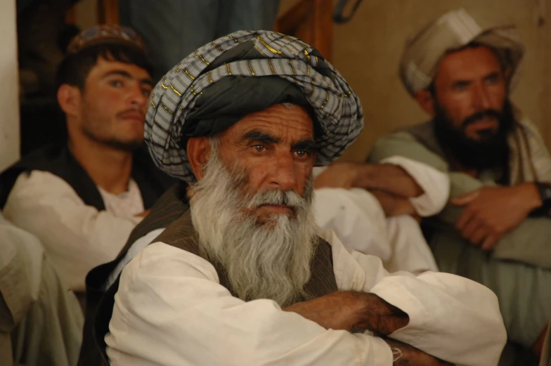 a man with gray beard and a white shirt is next to men in traditional clothing