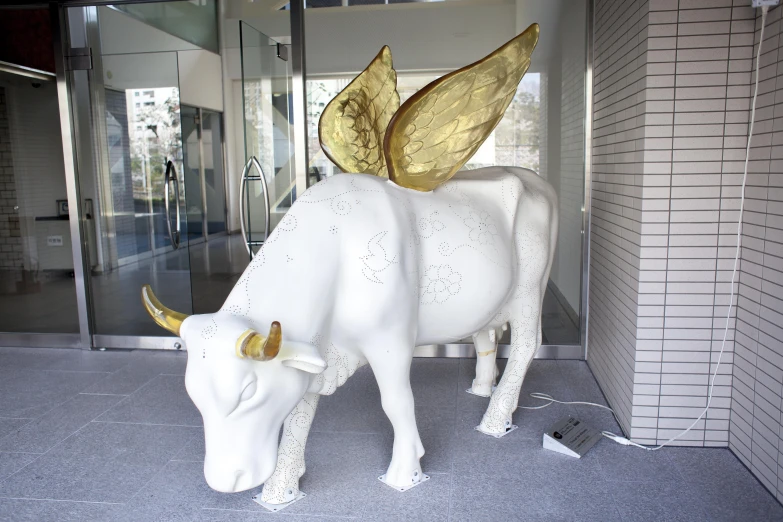 there is a white cow with gold horns standing in front of glass doors