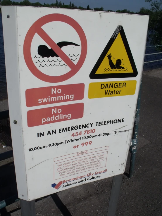 a sign warns not to swim into water while standing on a bridge