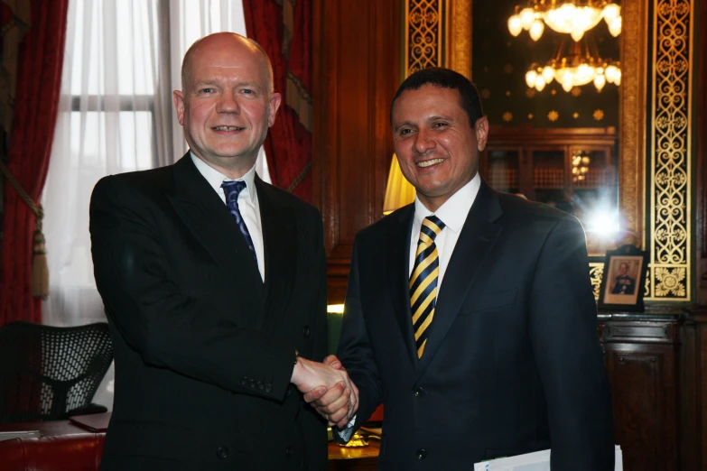 two men in suits shake hands inside a hall