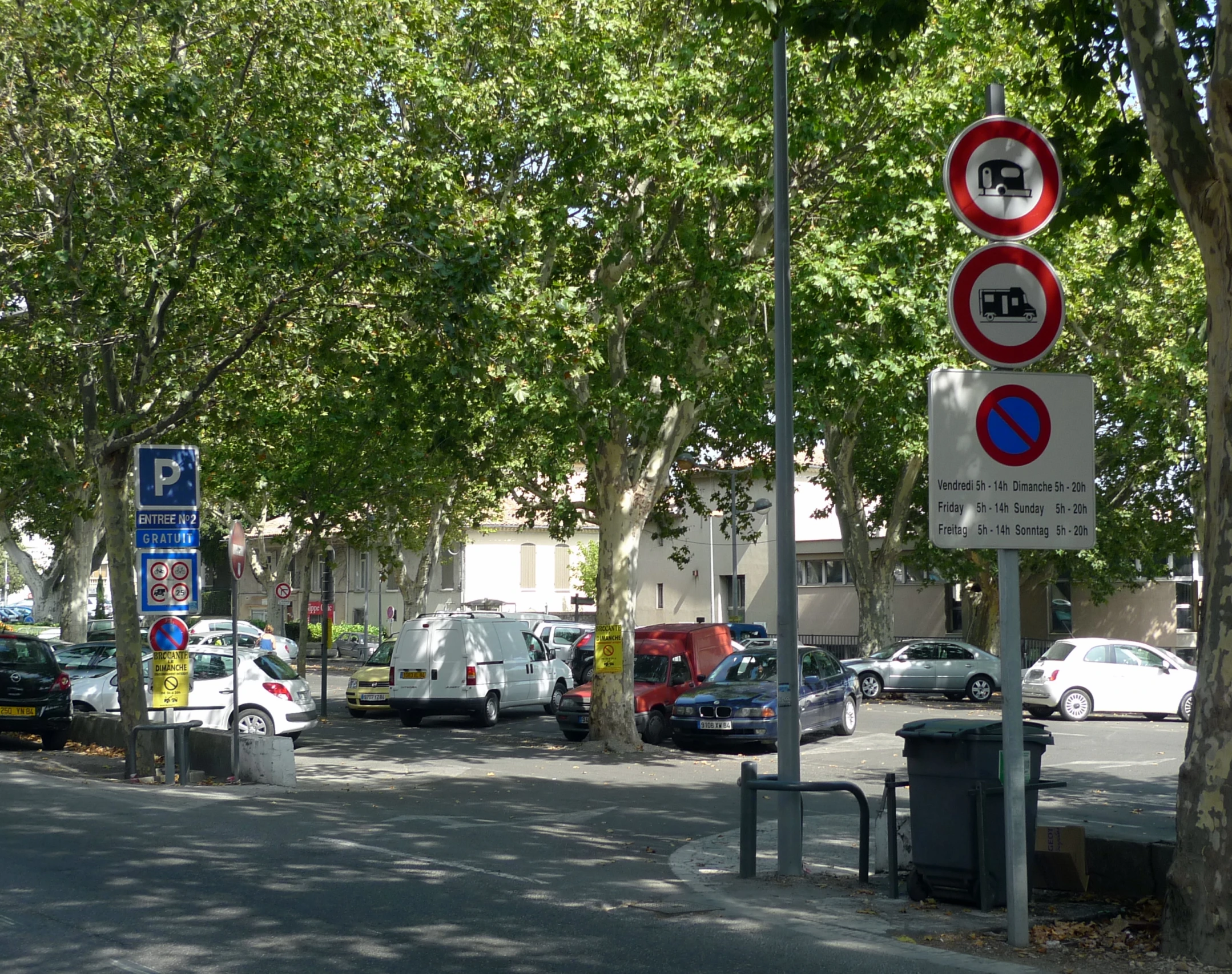 many cars are parked along the street next to some trees