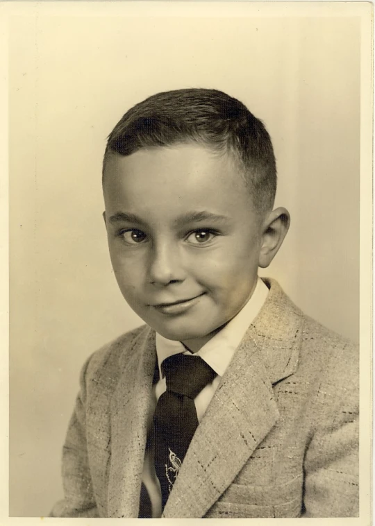 a little boy dressed in a suit and tie smiles at the camera