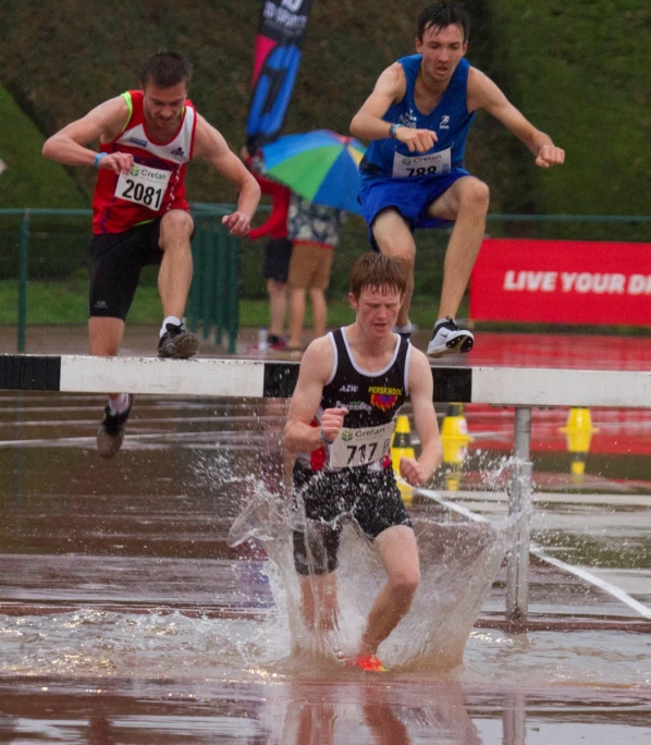 three men running in the rain with one jumping over the other