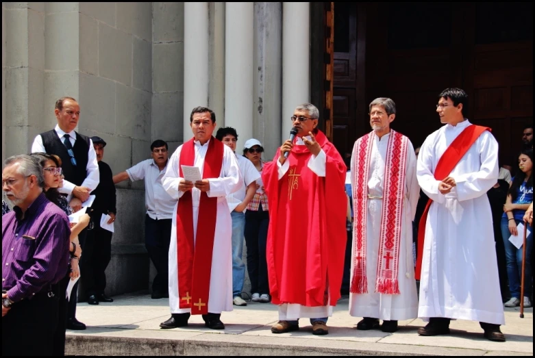 three priests are speaking with others in front of a large building