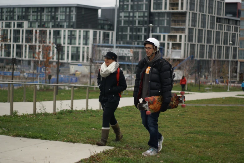 two people walk on the grass near tall buildings