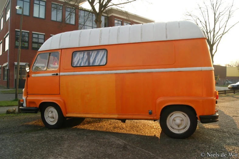 an orange and white vw van parked in front of a brick building