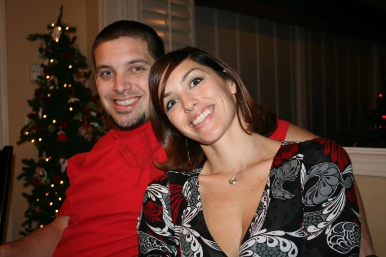 a couple is smiling with a christmas tree in the background