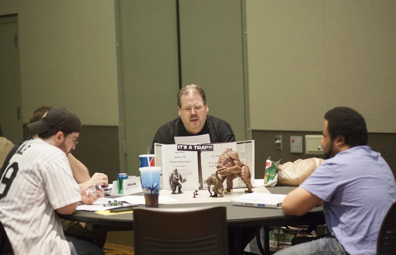 a man is sitting at a table with a comic book and other people