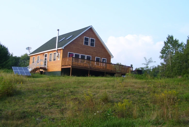 the house has a wooden deck overlooking a grassy field