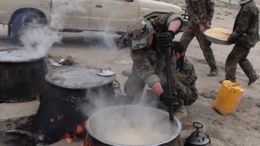 some soldiers cooking on a big pot of food