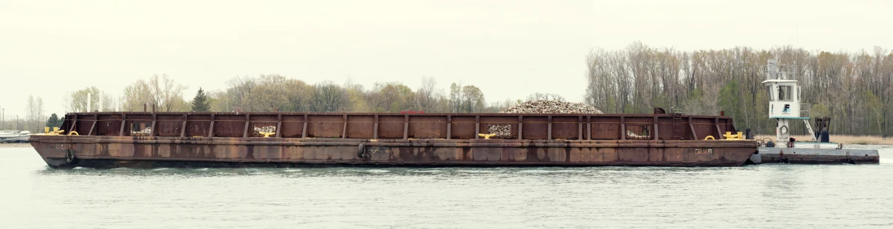 a brown and rusted barge traveling on a river