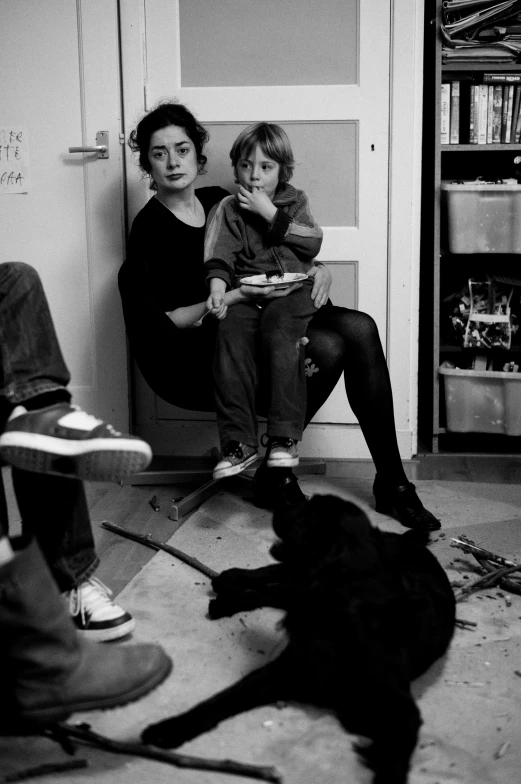 two women sit on chairs while one person holds a plate in the kitchen