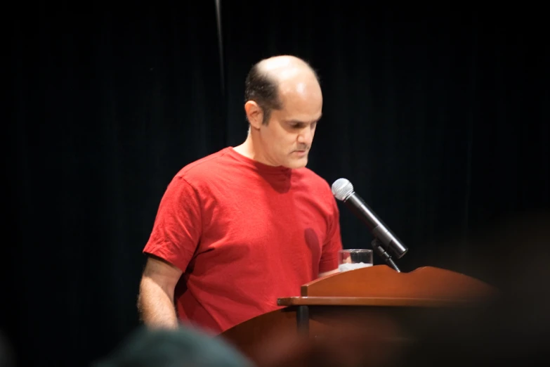 a bald man stands in front of a podium talking