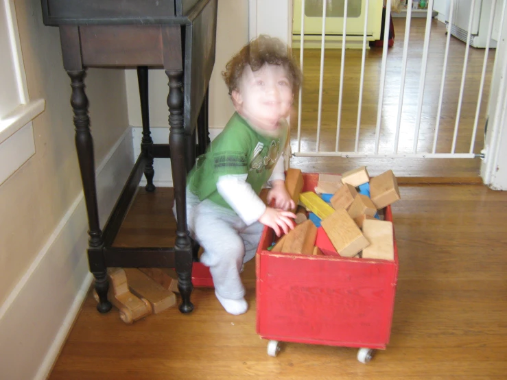 a baby sits in front of a cart that is filled with toys