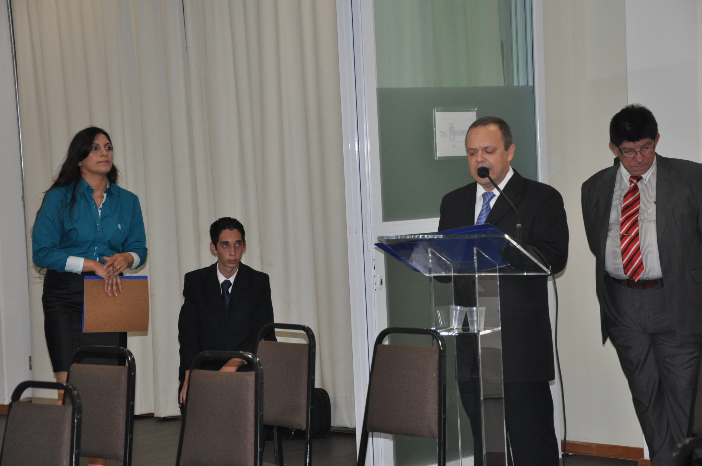 three men and one woman stand at podiums in suits