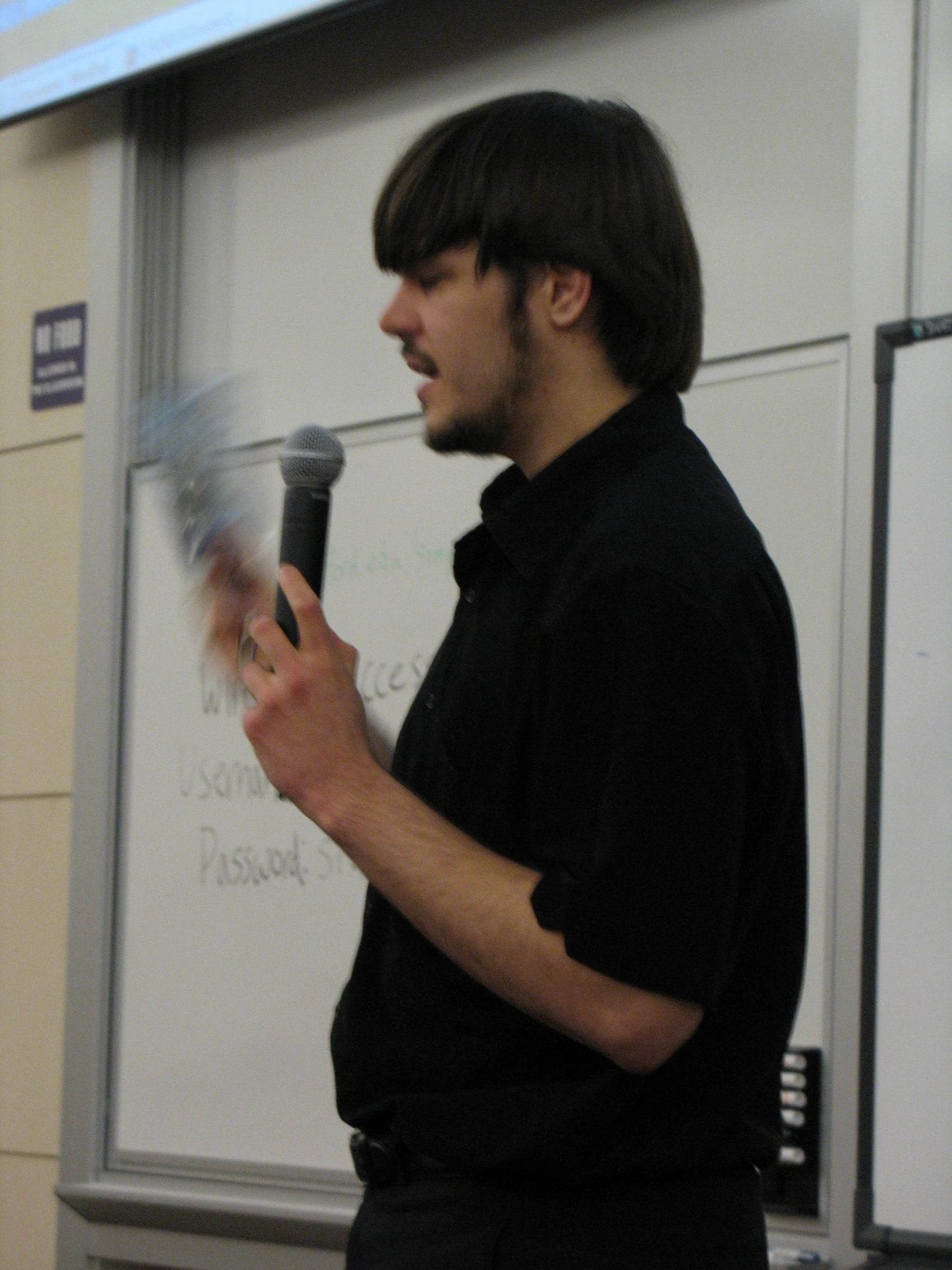 a man is holding a microphone and standing in front of a whiteboard
