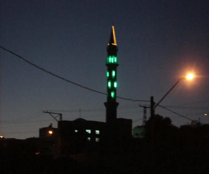 a clock tower lit up in the dark with a building in the background