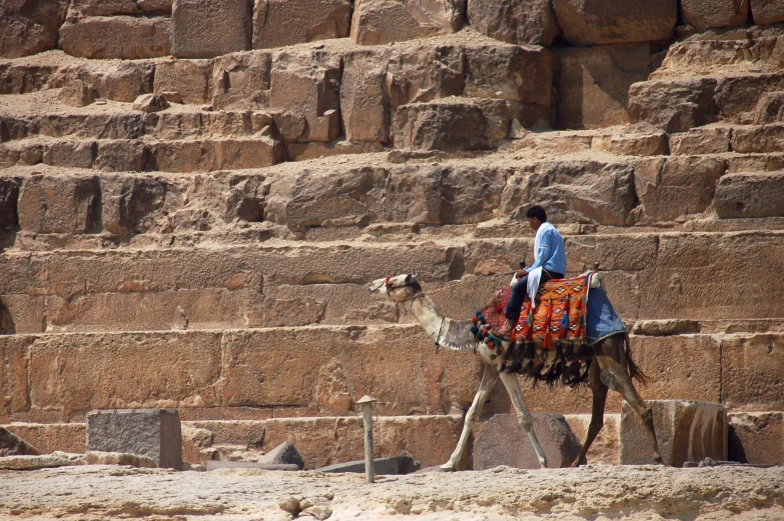 a man with a camel riding past two stone walls