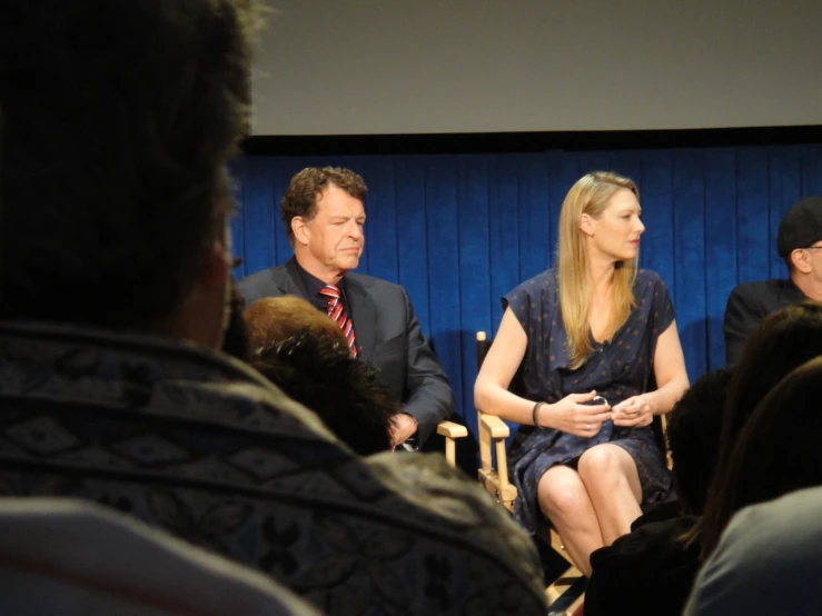 three people sitting on chairs while one man stands