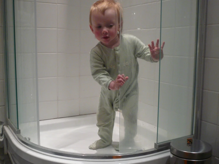 a young child standing in a shower wearing a bodysuit