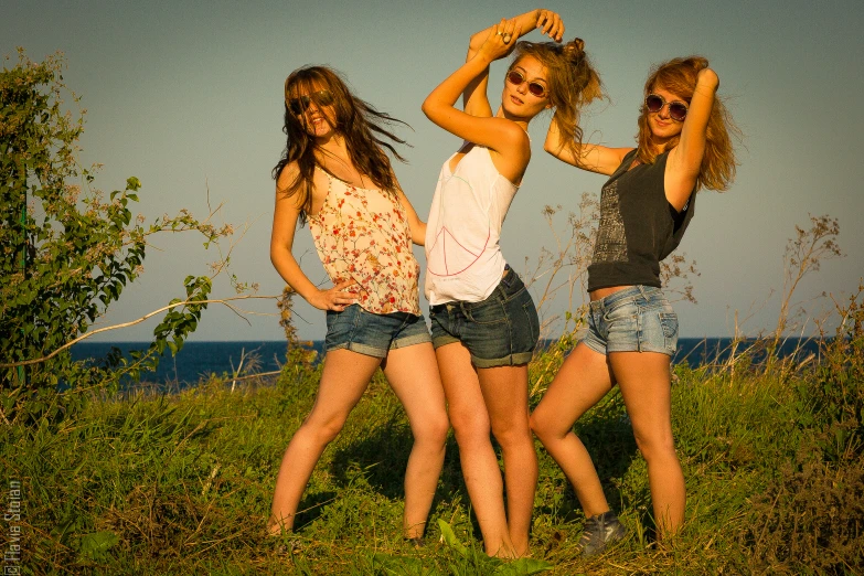 three girls pose on the grassy field in front of the ocean