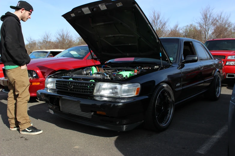 a young man stands near a modified car in the parking lot