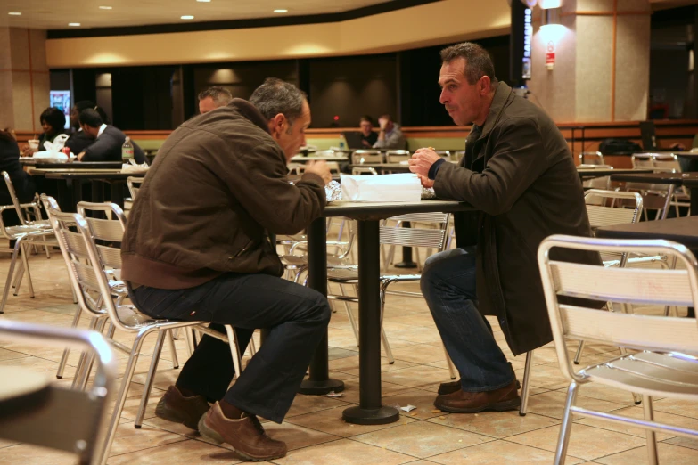 two men sit at a table at an indoor restaurant