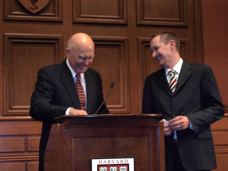 two men smile while standing at a podium