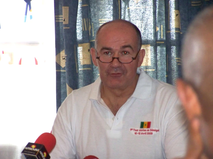 a man holding a microphone while sitting in front of two red microphones