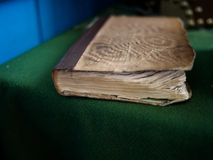 an old book sitting on a green table cloth