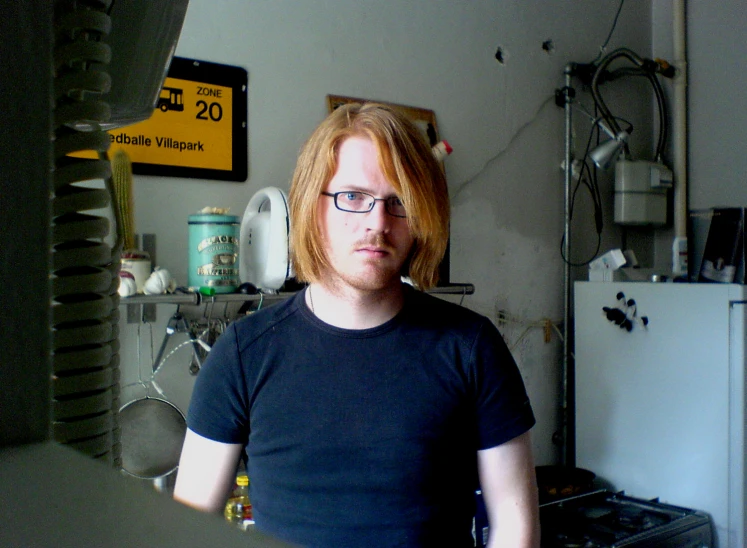 a man with glasses in a kitchen next to a fridge