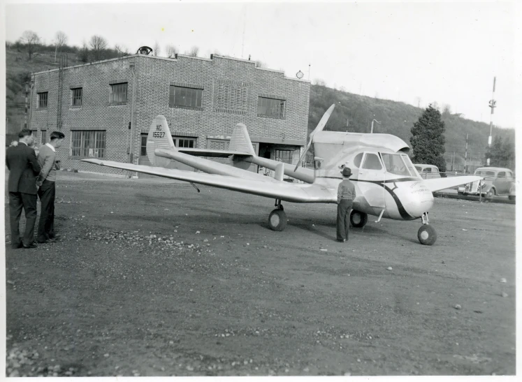 black and white po of small airplane parked in front of people