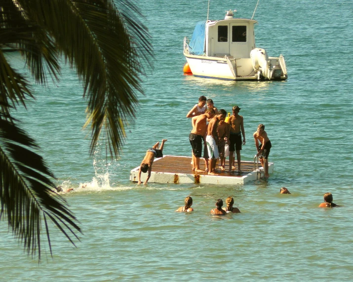 people standing and sitting in the water in front of a boat