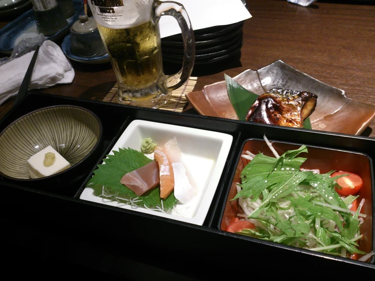 an open lunch compartment with two bowls, drinks, and salads