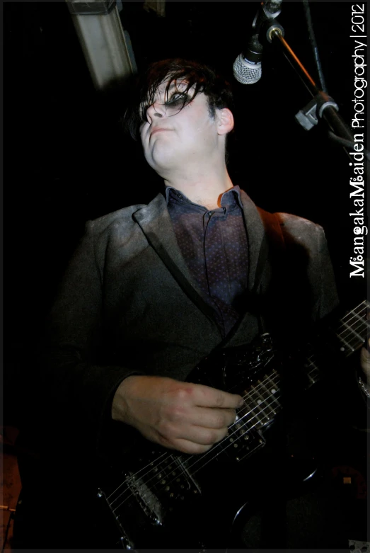 a young man playing a guitar in front of a microphone