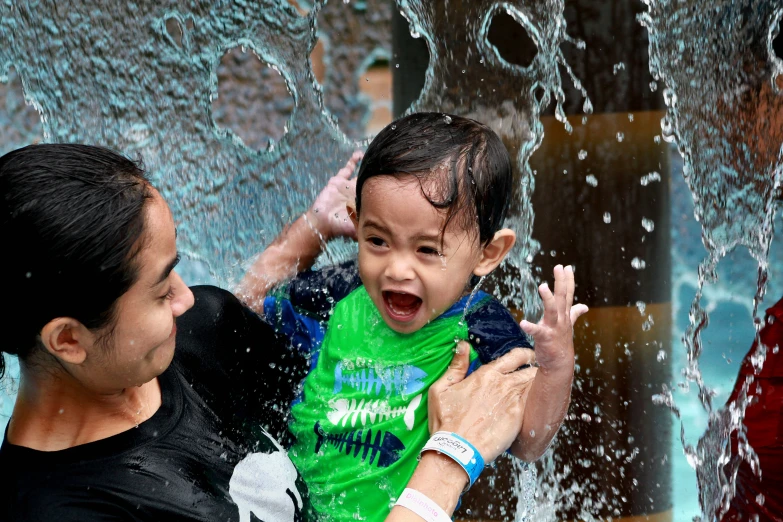 a boy plays in the water spraying from his father