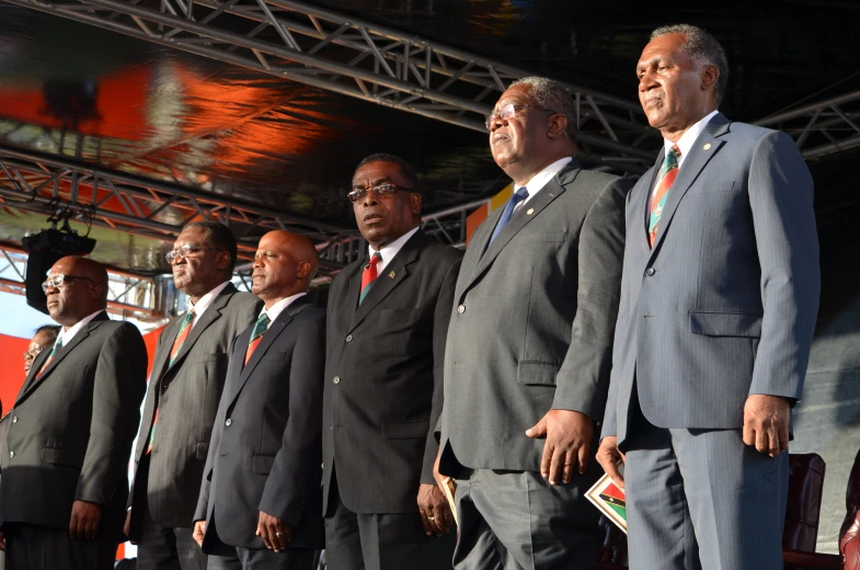 six men in suits stand in line on the side of the stage