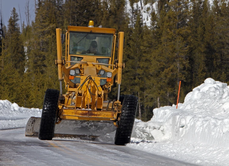 a yellow tractor in the snow and trees