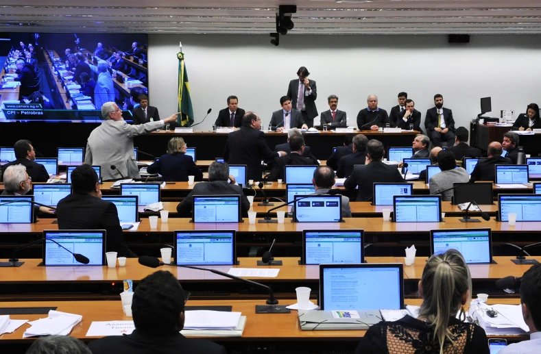 people sitting in rows using computers with projector screens on the wall