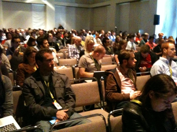 an auditorium full of people, many sitting down and there are some on their laptops