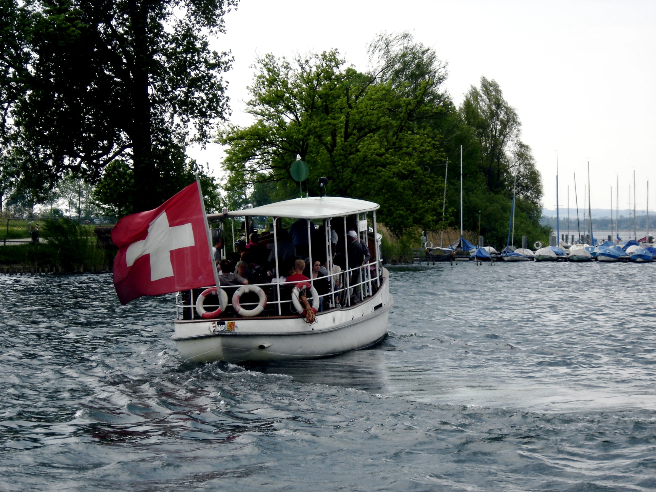 the small boat is carrying many people around a body of water