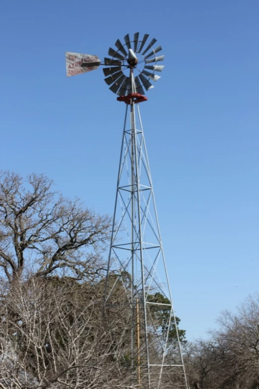 a tall pole windmill next to some trees