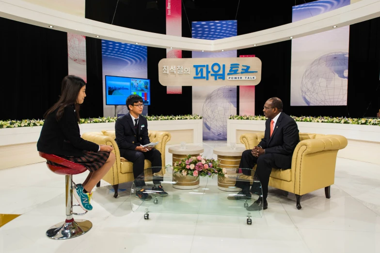 three people sit on sofas in front of two television screens