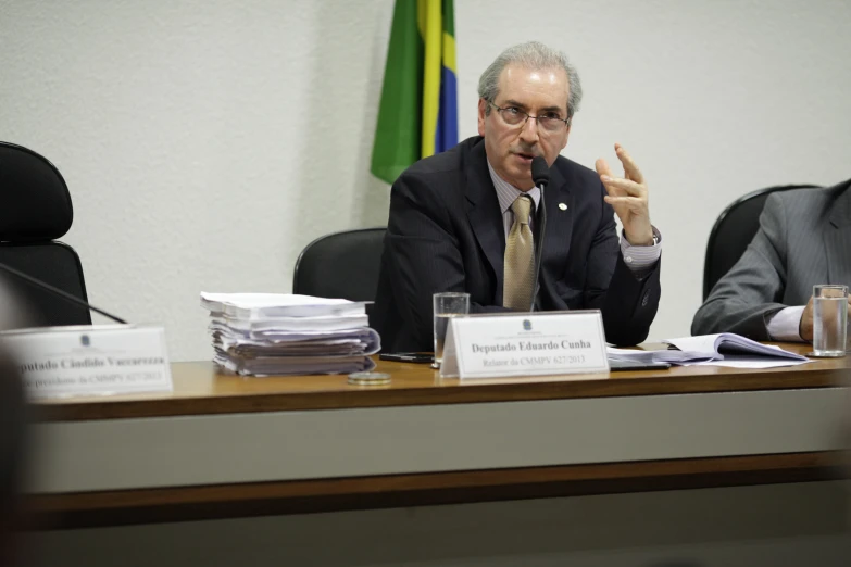 a man giving a peace sign sitting at a table with papers and drinks