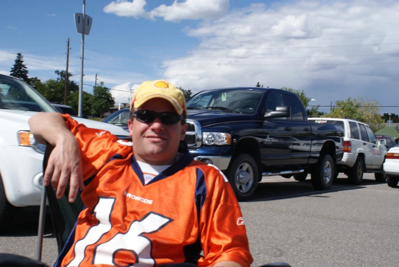 a man in an orange and white football jersey sits in front of other vehicles