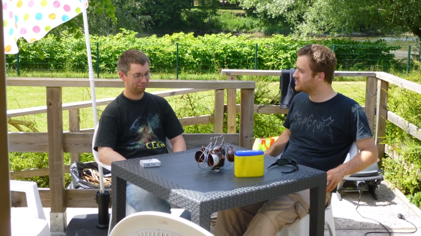 two men sit at a table talking in the back yard