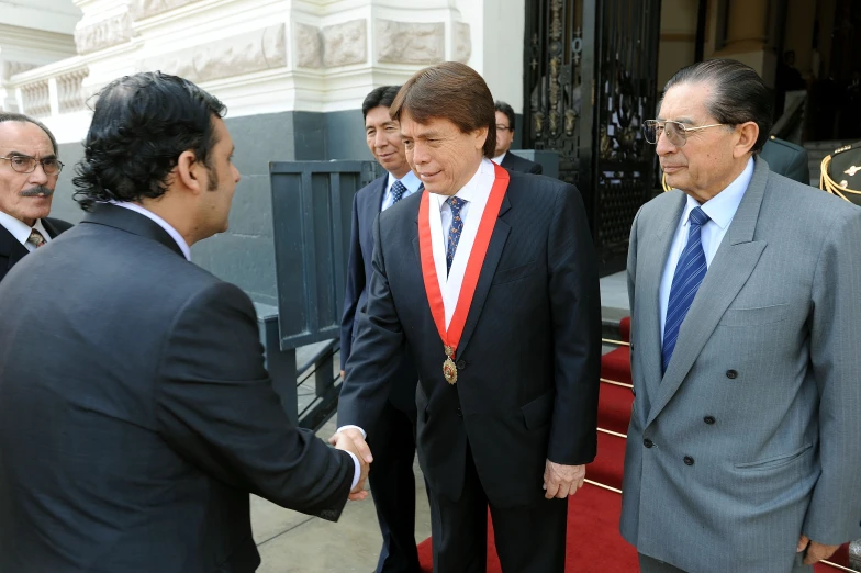 a man is shaking another person's hand and other men are in suits outside