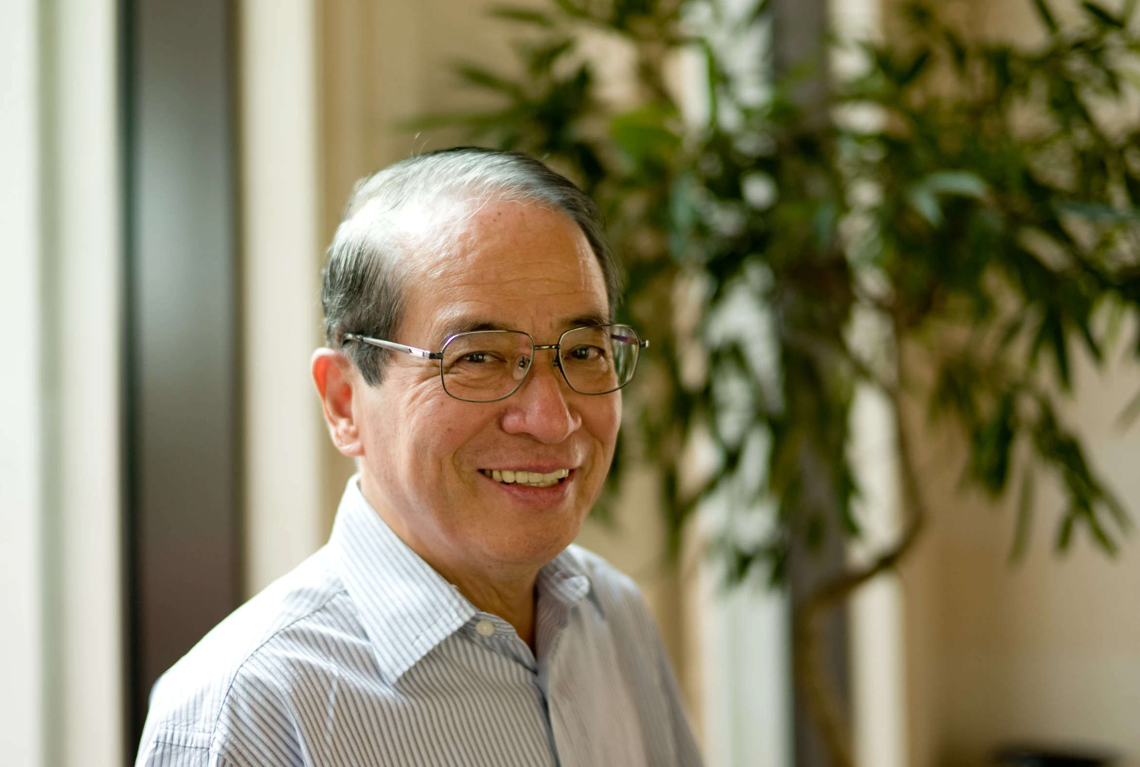 a smiling, older man standing in front of a house plant